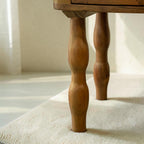 Homecrest Ravenna bedside table in natural acacia wood featuring unique curvy legs, placed on a wooden floor.