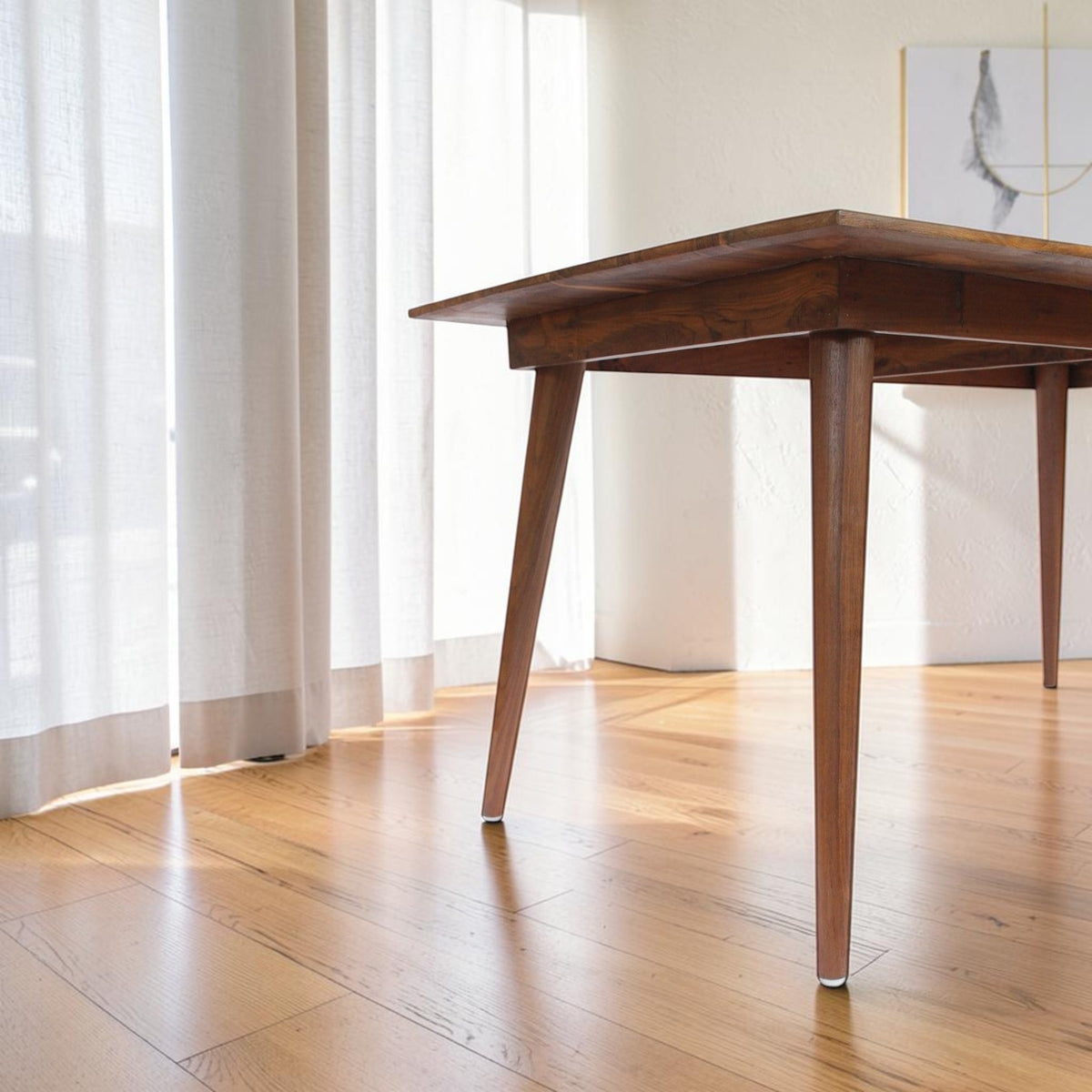 Homecrest Anders curved teak dining table with tapered legs in a bright, sunlit room with sheer curtains.