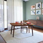 Homecrest Anders mid-century curved teak dining table in a warm wood finish set on a white rug in a modern room