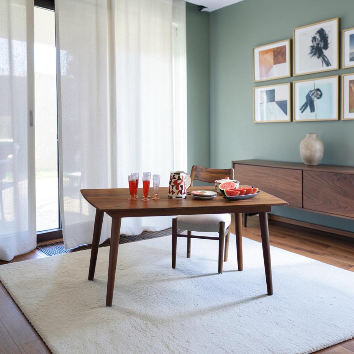 Homecrest Anders mid-century curved teak dining table in a warm wood finish set on a white rug in a modern room