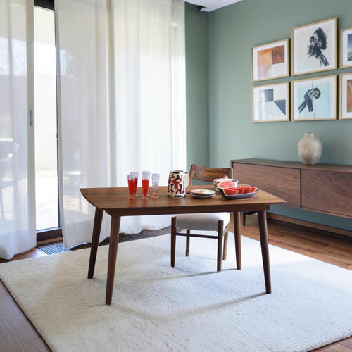 Homecrest Anders mid-century curved teak dining table in a warm wood finish set on a white rug in a modern room