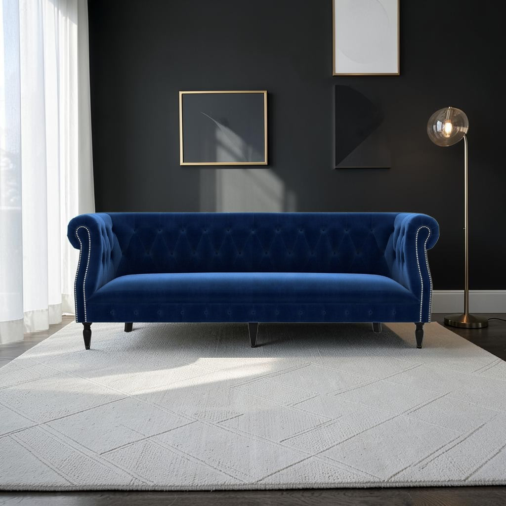 Homecrest Baslow Chesterfield sofa in indigo blue velvet with tufted back and silver nailhead trim on a white rug.