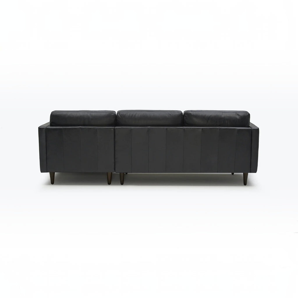 Homecrest Camber sectional sofa in rhino black leather with a deep boxy silhouette and dark wooden legs, back view.