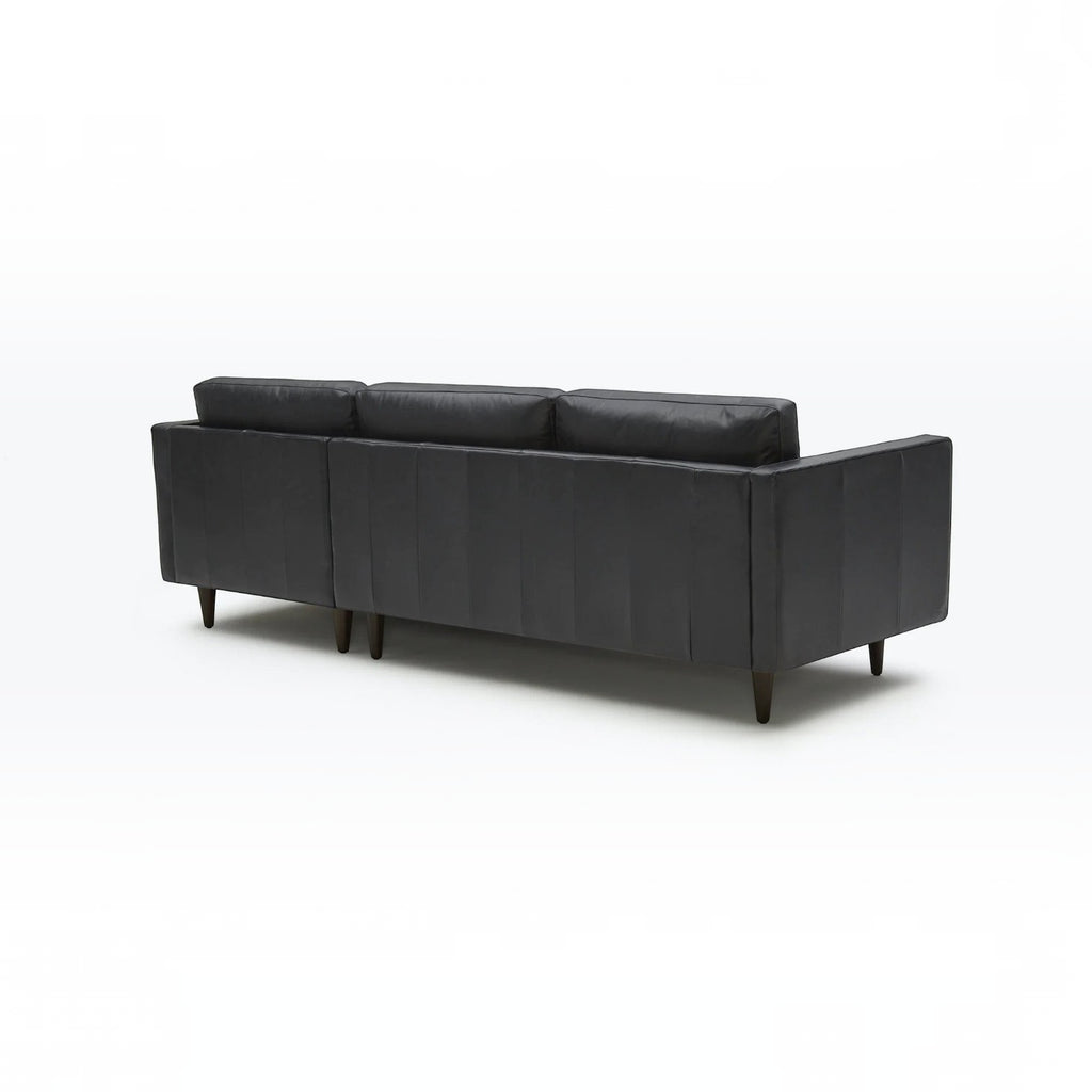 Homecrest Camber sectional sofa in rhino black leather with a boxy silhouette and tapered wooden legs, back view.