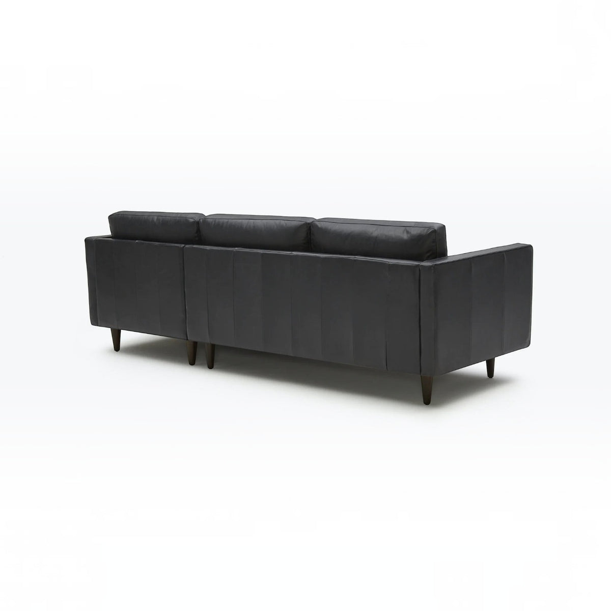 Homecrest Camber sectional sofa in rhino black leather with a boxy silhouette and tapered wooden legs, back view.