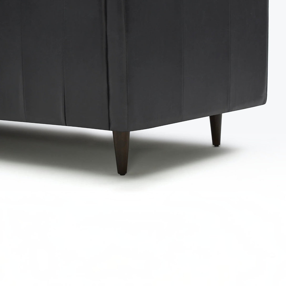 Homecrest Camber sectional sofa in rhino black leather with tapered dark wood legs on a white background