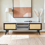 Homecrest Calder black media cabinet with rattan doors, gold handles, and open shelving in a bright living room.