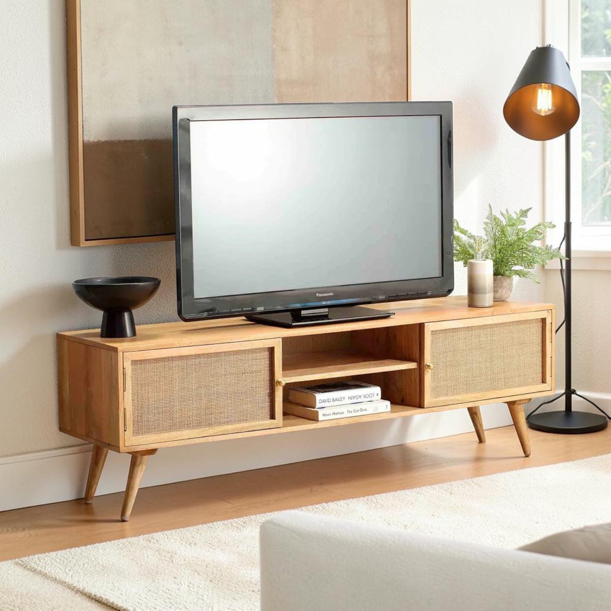 Homecrest Calder media cabinet in natural mango wood with rattan doors, gold handles, and open central shelving.