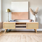 Homecrest Calder media cabinet in natural mango wood with rattan doors, gold handles, and open central shelving.