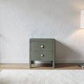 Homecrest Cranham bedside table in olive green hardwood with two drawers and round white knobs against a textured wall.