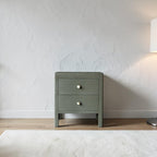Homecrest Cranham bedside table in olive green hardwood with two drawers and round white knobs against a textured wall.
