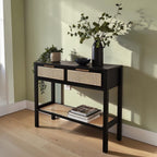 Homecrest Corvin black mango wood console table with two rattan cane drawers and a lower shelf against a green wall