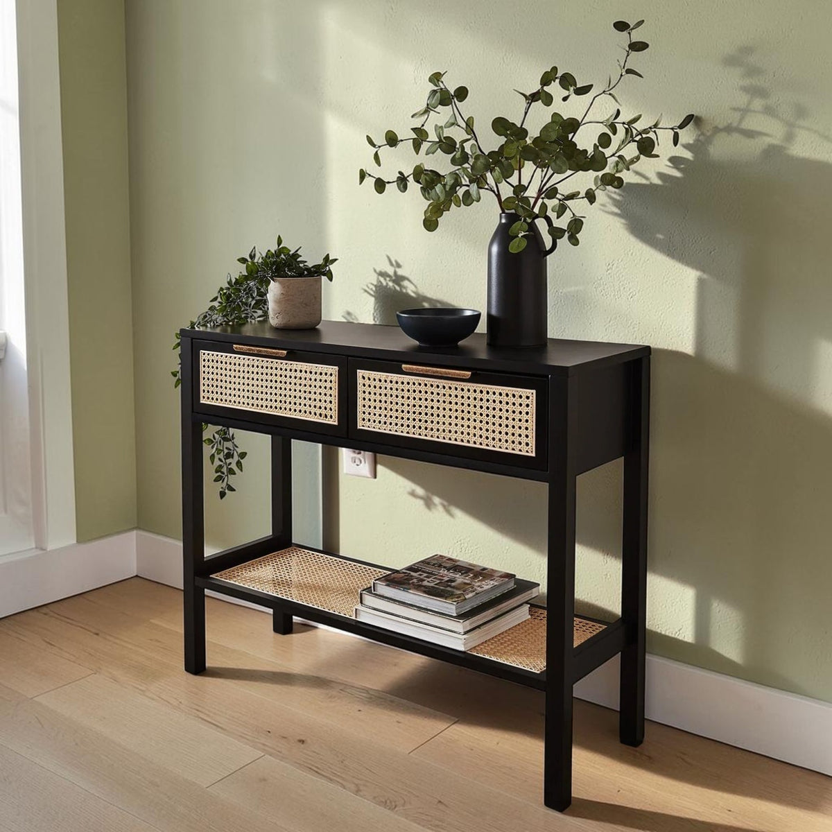 Homecrest Corvin black mango wood console table with two rattan cane drawers and a lower shelf against a green wall