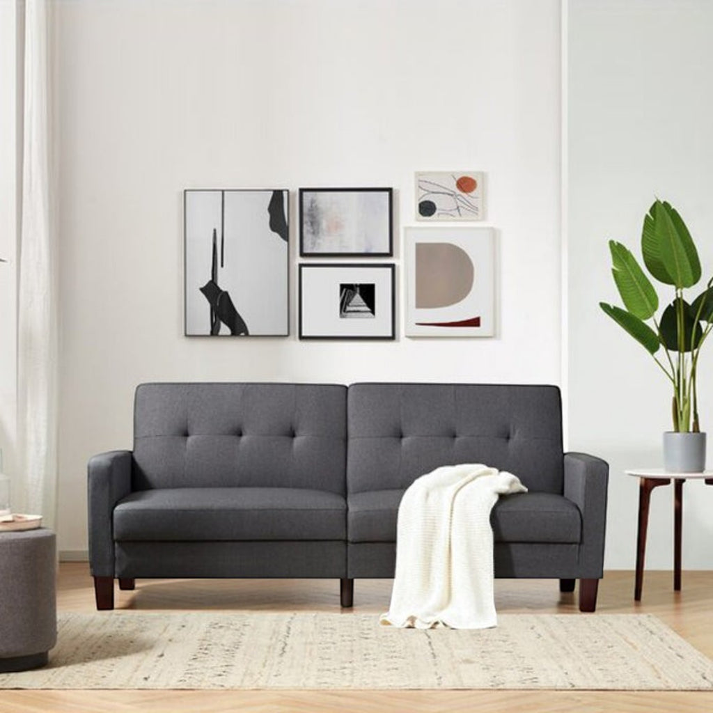 Homecrest Delaney dark grey three-seater sofa bed with tufted backrest and solid wood frame in a modern living room.
