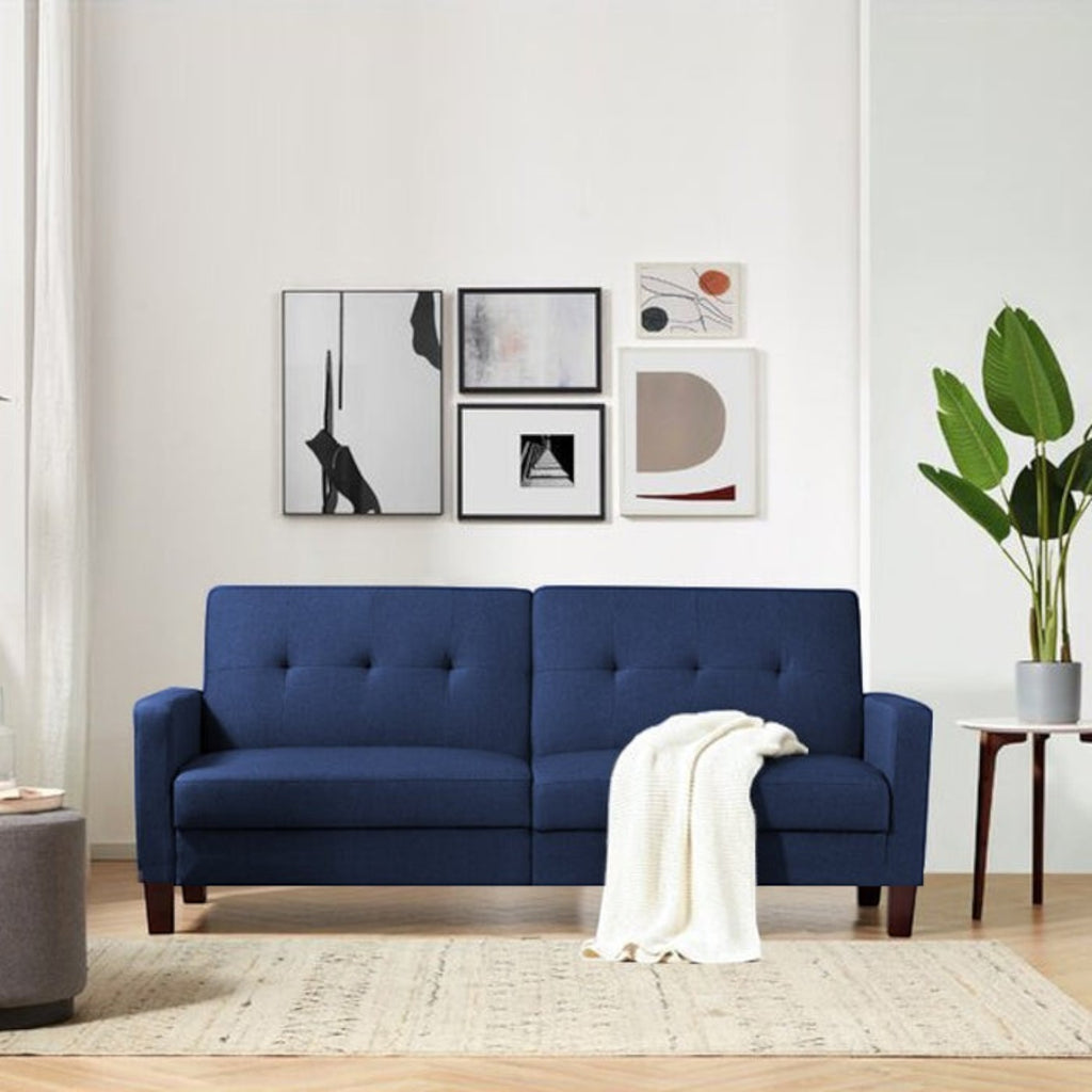 Homecrest Delaney navy blue three-seater sofa bed with tufted backrest and solid wood frame in a modern living room.
