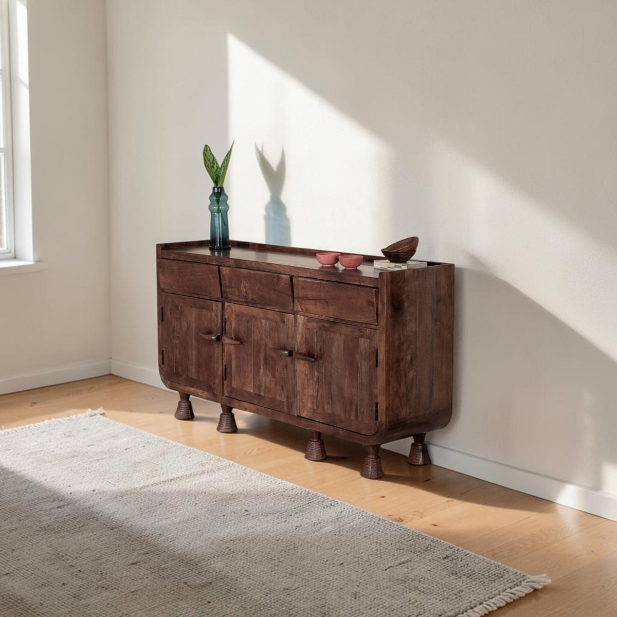Homecrest Fairholm walnut acacia wood sideboard with contoured shutter doors and unique pedestal legs in a bright room