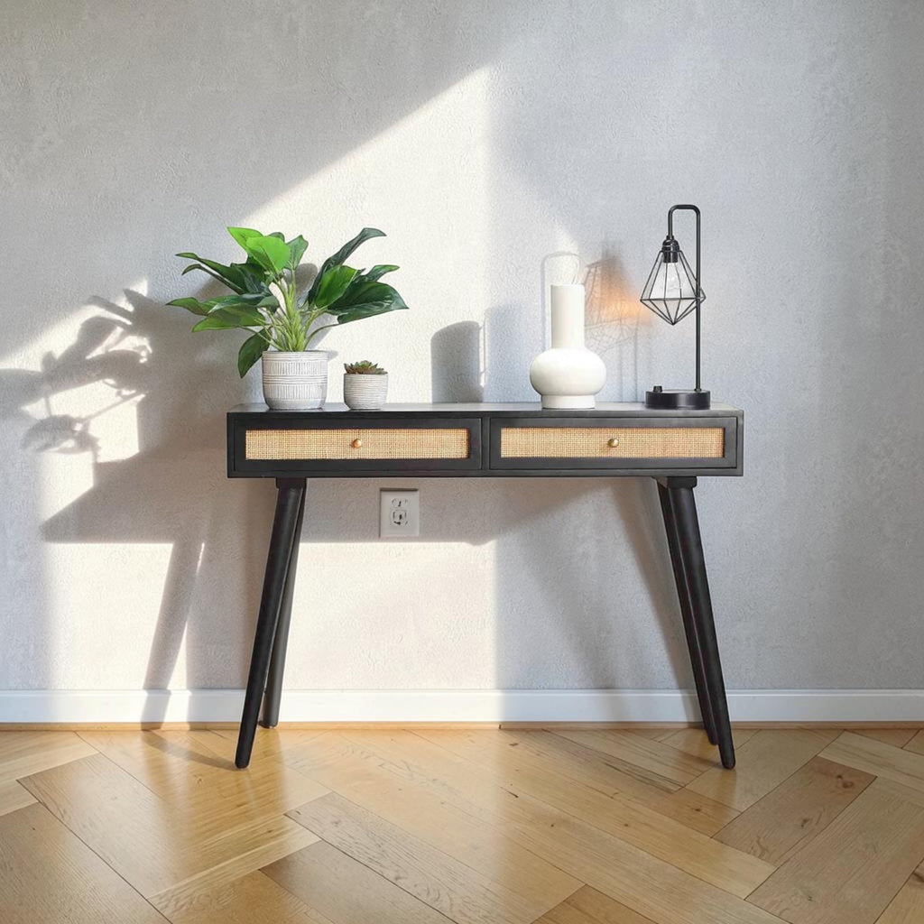 Homecrest Isla black hallway console table with two woven rattan cane drawers and gold handles against a grey wall.