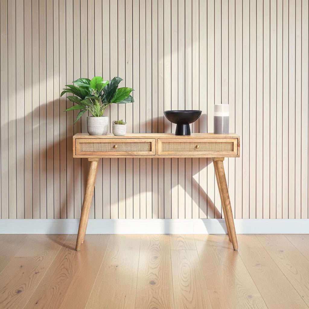 Homecrest Isla natural wood console table with two woven rattan cane drawers and gold handles against a slat wall