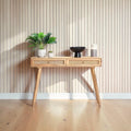 Homecrest Isla natural wood console table with two woven rattan cane drawers and gold handles against a slat wall