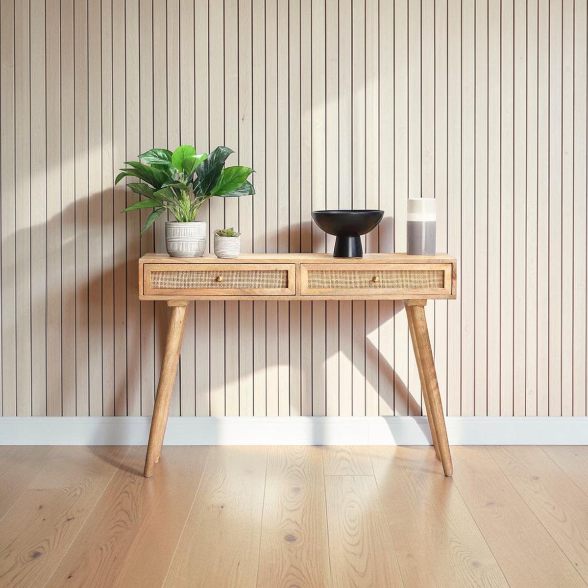 Homecrest Isla natural wood console table with two woven rattan cane drawers and gold handles against a slat wall