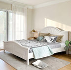 Homecrest light beige Sheesham wood bed with a curved headboard and decorative wreath carving in a bright bedroom