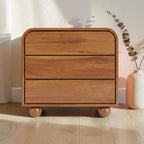 Homecrest Brisley 3-drawer chest in brown acacia wood with a rounded frame and spherical feet in a bright room.