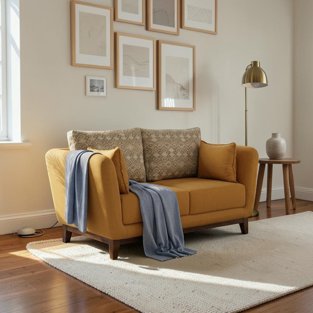 Homecrest 2-seater sofa in mustard fabric with patterned back cushions, curved armrests, and a light blue throw blanket.