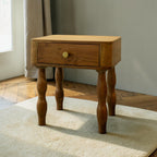 Homecrest Ravenna bedside table in natural acacia wood with a single drawer and unique curvy legs on a cream rug.