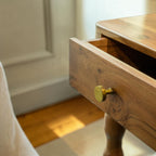 Homecrest Ravenna bedside table in natural acacia wood with a single drawer and brass knob in a coastal bedroom