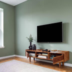 Homecrest Rowley solid wood media cabinet in a honey finish with open shelving, styled in a sage green living room.