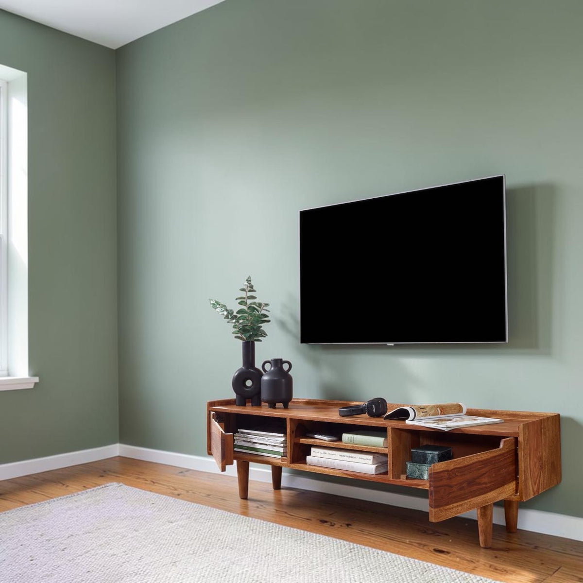 Homecrest Rowley solid wood media cabinet in a honey finish with open shelving, styled in a sage green living room.