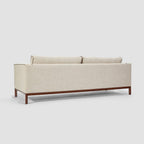 Homecrest Solace deep-seat lounge sofa in ivory fabric with contrast piping on a dark teakwood base, rear view.