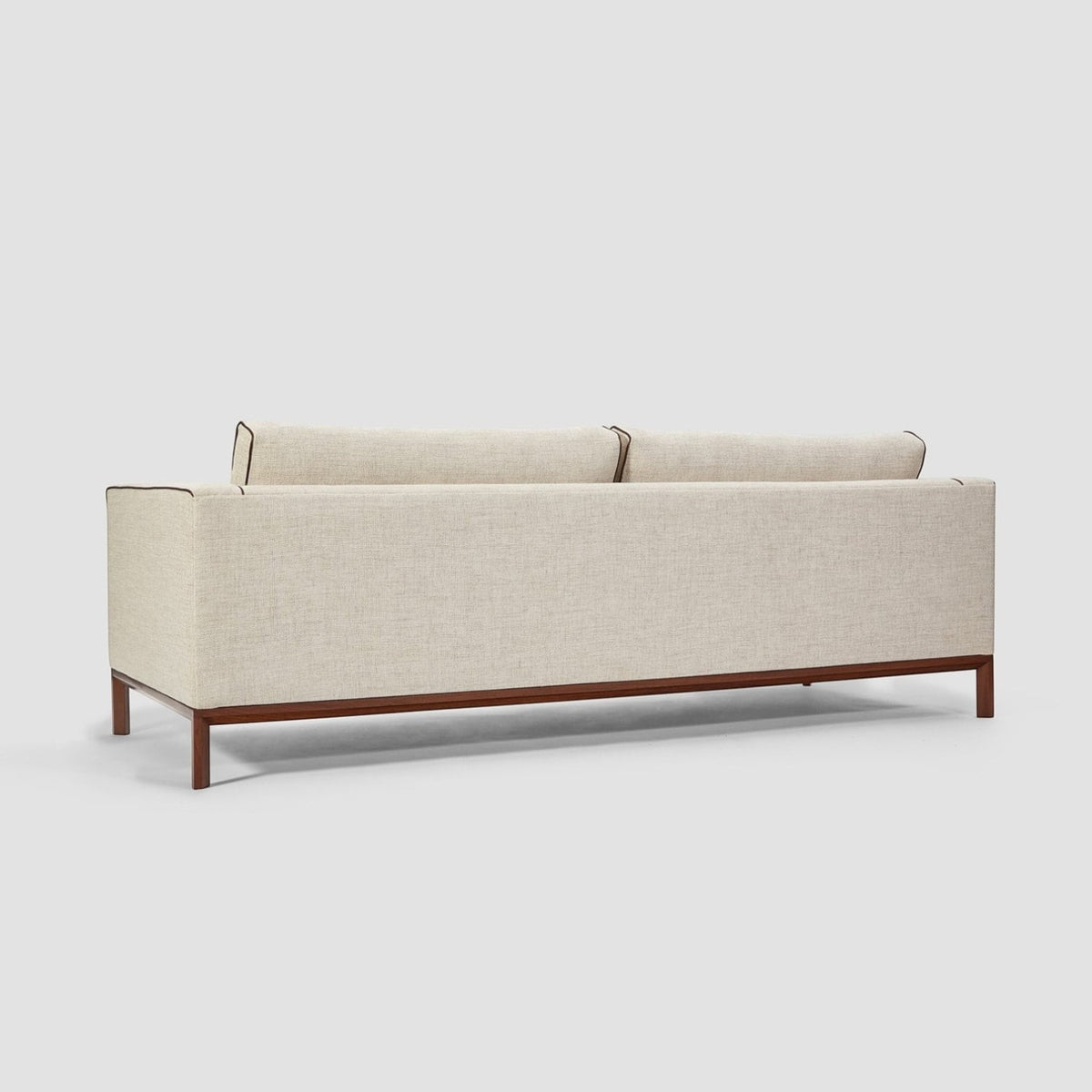 Homecrest Solace deep-seat lounge sofa in ivory fabric with contrast piping on a dark teakwood base, rear view.