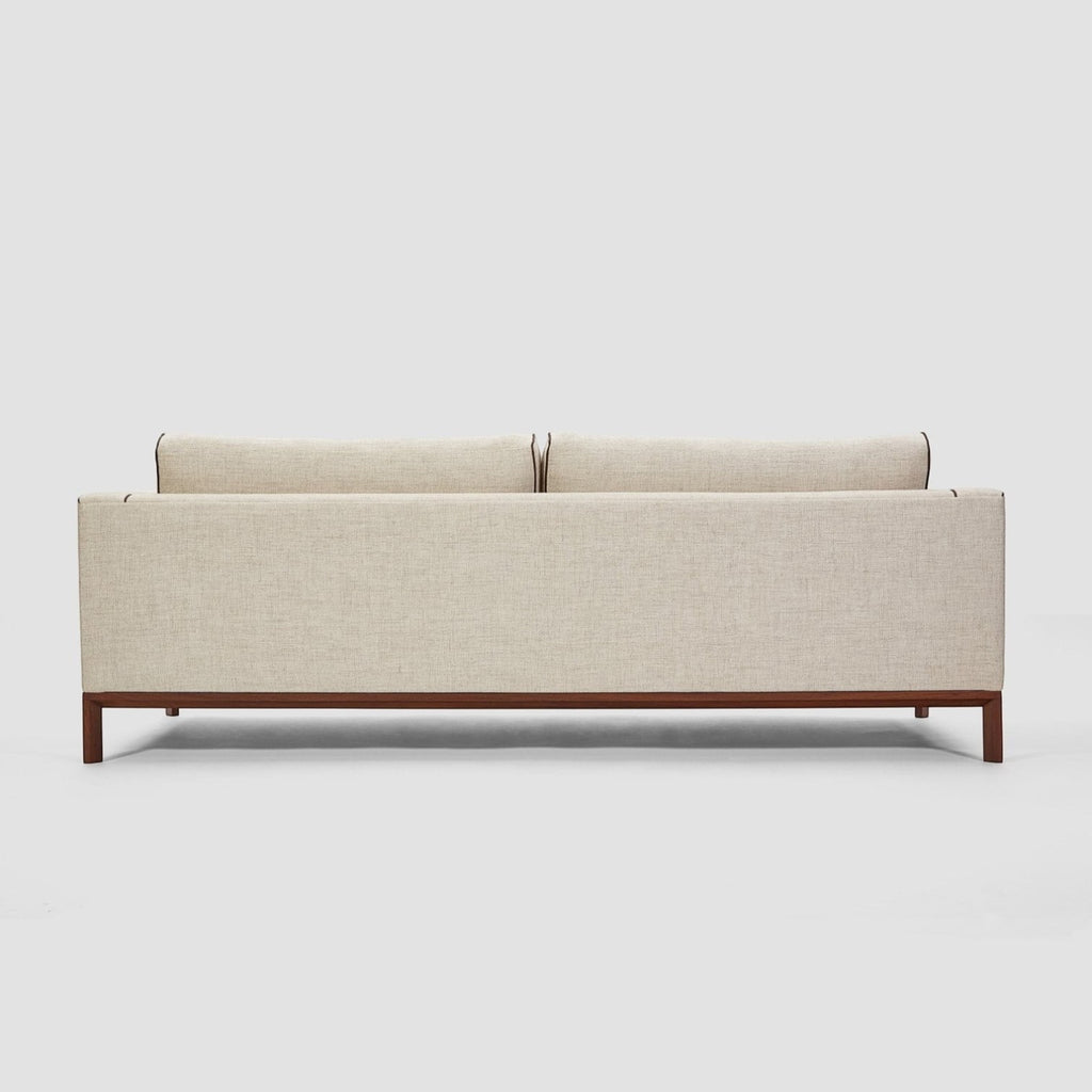 Homecrest Solace deep-seat lounge sofa in ivory fabric with brown contrast piping on a teakwood base, back view.