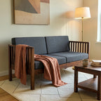 Homecrest contemporary solid wood sofa with dark grey cushions, slatted arms, and a draped terracotta throw blanket.
