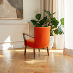 Homecrest Pelham armchair in vibrant orange fabric with a mid-century modern teak wood frame in a sunlit living room.