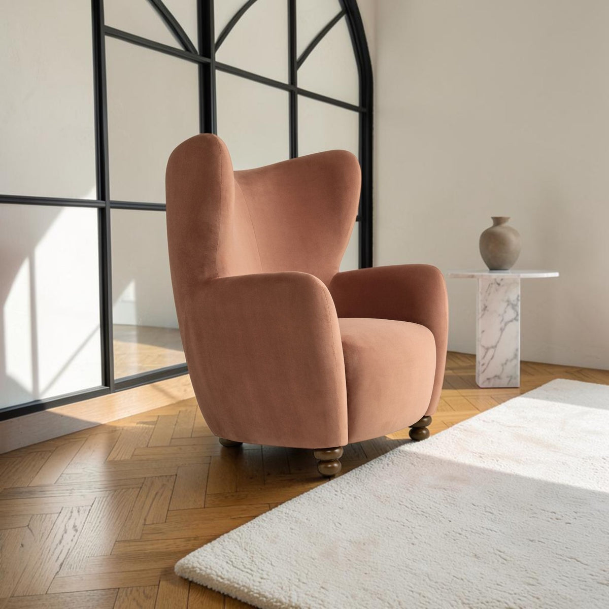 Homecrest Yannick wing-arm accent chair in truffle pink velvet with dark turned wooden feet in a bright room.
